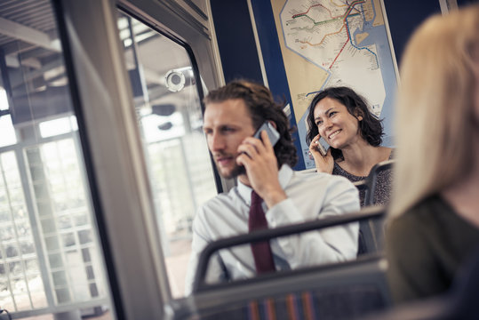 Two people seated on a bus talking on their cell phones