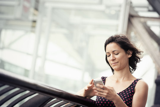 A woman standing outside a building checking her cell phone. 