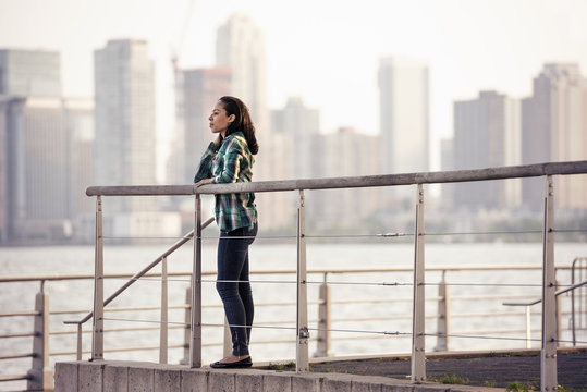 A woman standing on the waterfront, view to the city over the water in New York City. 