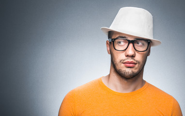 Portrait of trendy young man, isolated on gray. Close up gorgeous guy with hat and eyeglasses looking to side. Copyspace