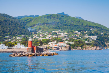 Red lighthouse tower on stone breakwater. Ischia