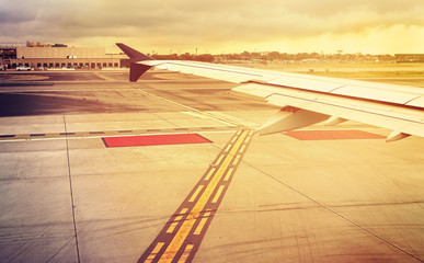 Vintage toned plane wing above runway at sunset, travel concept.