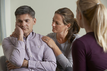Mature Couple Talking With Counsellor As Woman Comforts Man
