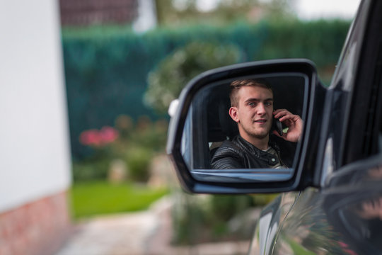 portrait of young adult behind steering wheel inside a car making a phone call with his smartphone