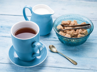 Cup of tea, milk jug and cane sugar cubes.