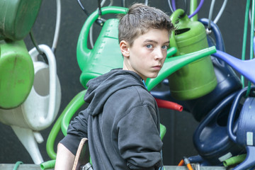 portrait of a teenage boy in front of hanging watering cans