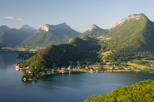 Bewaldete Bergr&uuml;cken und Felsen am Lac d'Annecy leuchten in der Morgensonne