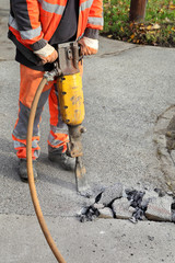 Worker at construction site demolishing asphalt with pneumatic plugger hammer