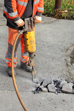 Worker at construction site demolishing asphalt with pneumatic plugger hammer