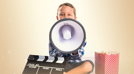 Kid with clapperboard and popcorns shouting by megaphone
