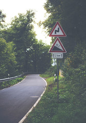A dangerous road ahead. An image of a warning signs for curvy road ahead with huge altitude change for 15% for next 2km. Focus point is on the warning signs. Image has a vintage effect applied.