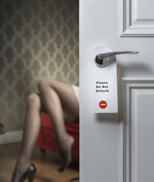 Hotel door with do not disturb icon and sexy female legs on the background; adultery concept
