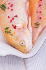 golden trout on a baking dish with red pepper and thyme. gold fish. home kitchen.