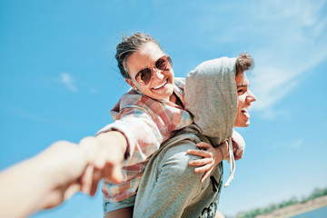 Happy loving couple. Happy young man piggybacking his girlfriend. Cheerful laughing hipsters on blue sky background