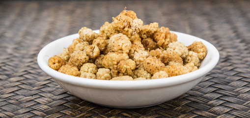 Dried white mulberry in a white bowl over wicker background