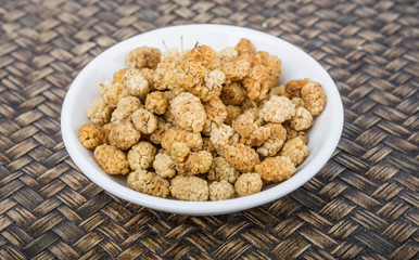 Dried white mulberry in a white bowl over wicker background