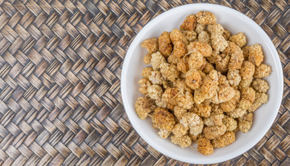 Dried white mulberry in a white bowl over wicker background
