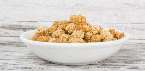 Dried white mulberry in white bowl over wooden background