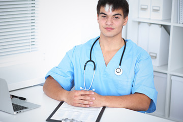 Portrait of unknown male surgeon doctor sitting at the table in hospital office, stethoscope