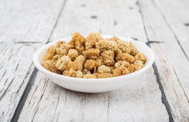Dried white mulberry in white bowl over wooden background