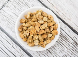 Dried white mulberry in white bowl over wooden background