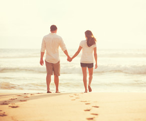 Fototapeta na wymiar Young Lovers Walking Down the Beach at Sunset