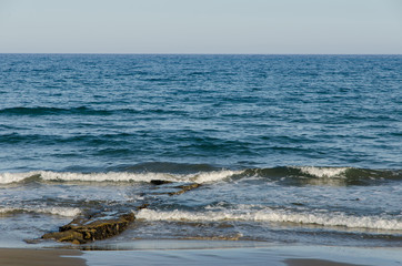 small waves of the sea crushing into a long stone structure on the sand beach