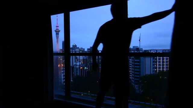 Man looking out window with aerial urban view of Auckland city skyline at dusk