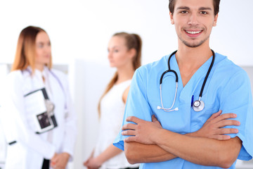 Attractive male doctor in front of medical group, crossed arms