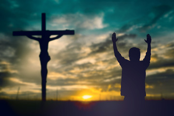 Silhouette of man with raised hands over blur cross concept for
