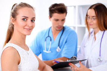 Fototapeta premium Happy blond female patient next to a few doctors in hospital sitting at the table