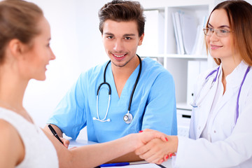 Fototapeta premium Attractive male doctor surgeon near female doctor and patient shaking hands, sitting at the table