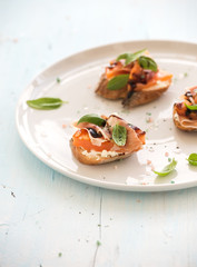 Bruschettas with Prosciutto, roasted melon, soft cheese and basil on white ceramic plate over light blue background