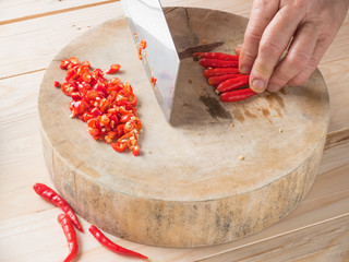Hand chopping chili on chopping block on wood background with co