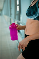 female hand holding pink bottle of water, taking a break from exercise in modern bridge construction 