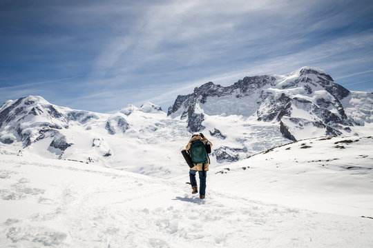 A man in camouflage winter coat and backpack standing in front of the background of snow mountain.