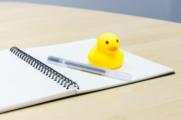 Pen and notebook and Rubber Duck on wooden desk