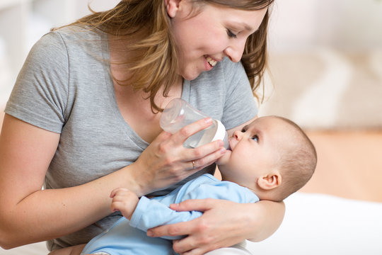 Cute Mother At Home Feeding Baby With A Milk Bottle