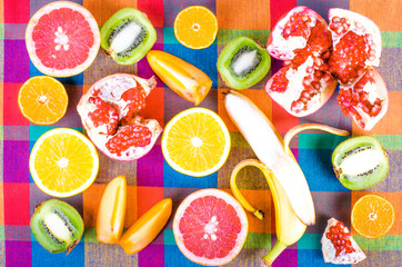 Fresh fruits on a colorful checkered kitchen towel. Raw and vegetarian eating background. Sliced orange, persimmon, kiwi, tangerine, banana, lemon, apple,  grapefruit, pomegranate, lime,  Top view