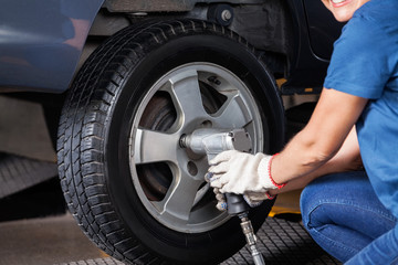 Female Mechanic Using Pneumatic Wrench To Fix Car Tire
