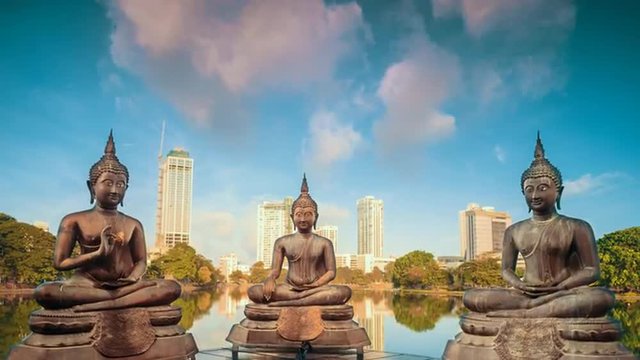 Bronze statues of benevolent Buddhas sitting in meditation on the modern city by the lake background timelapse at sunrise time.