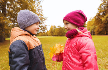 little boy giving autumn maple leaves to girl