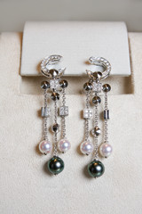 Luxury earrings made of white gold with diamonds and perls on a stand.