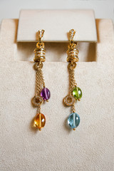Luxury earrings made of yellow gold with diamonds and precious colorful gems on a stand