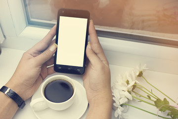 The woman is drinking coffee, phone in hand