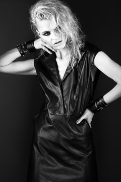 Daring girl model in black leather dress, style of rock, dark make-up, wet hair and bracelets on her arms.