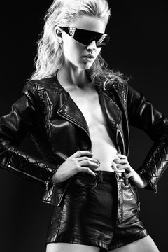 Daring girl model in fashion sunglasses, leather black clothes on naked body, dark make-up, wet hair. style rock.  Black-and-white image.