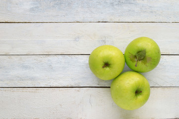 Three ripe green apples. Natural fruit with leaves on a white wooden table. Empty copy space for editor's text.