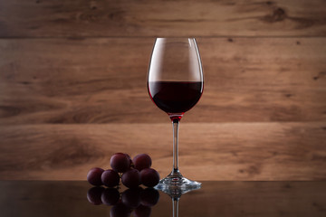 Drink and food. Wineglass, with red  wine and red grapes on wooden texture