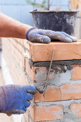Construction mason worker bricklayer installing red brick with trowel putty knife outdoors